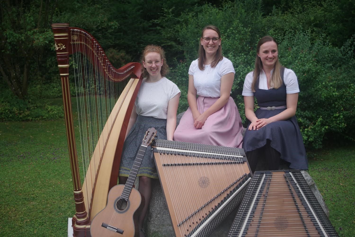 Drei Frauen in Tracht stehen hinter ihren Instrumenten (Harfe, Gitarre und zwei Hackbrettern)